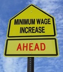 Picture of yellow road sign with pointed top stating "Minimum Wage Increase Ahead"