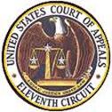 Badge for the Eleventh Circuit United States Court of Appeals: Round circle with a black outer line and a yellow inner line, then an inner white ring with black letters all capped on the top arch “UNITED STATES COURT OF APPEALS” and black letters all capped on the bottom arch “• ELEVENTH CIRCUIT •”, and inside that ring is a picture of a bald eagle with his wings opened in a ¾ stance behind gold scales of justice weighing a silver star on each side with a gold ribbon along with bottom arch