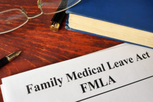 Picture of FMLA Family Medical Leave paper on desk next to blue book and a pair of glasses