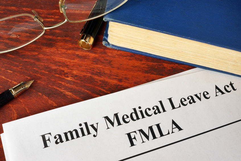 Picture of FMLA Family Medical Leave paper on desk next to blue book and a pair of glasses