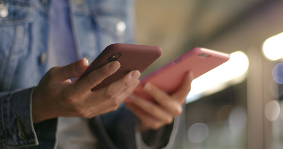 Picture of two cell phones one held in each hand of the same person