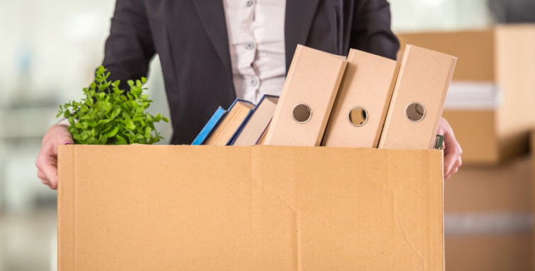 young businesswoman leaving work holding cardboard box with her things.