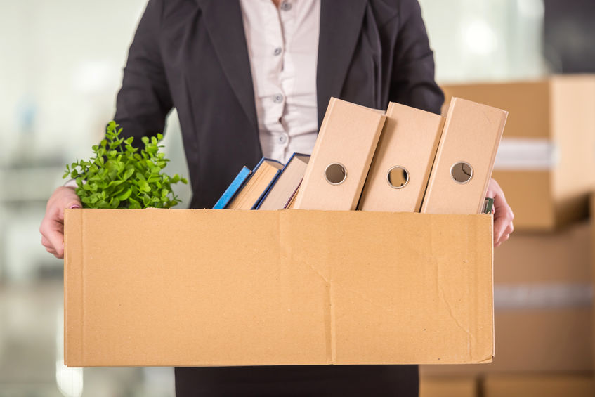 Picture of a woman holding a cardboard box of files, bocks and a plan as she packs up her desk fired