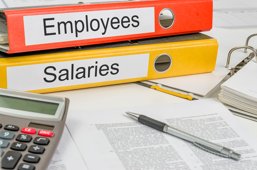 Picture of a desk with papers a calculator pen and notebooks, a red notebook with Employees and a Yellow notebook with Salaries