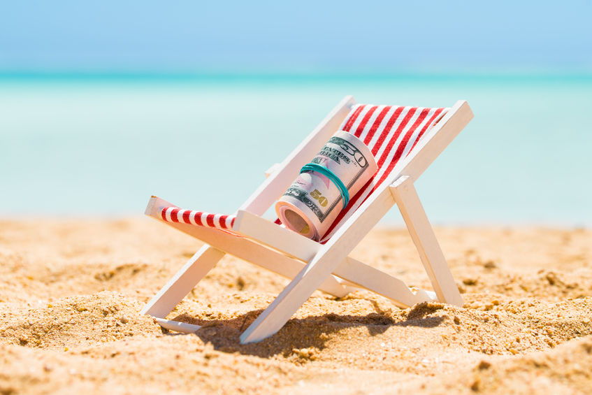 Picture of a wooden lounge chair on the beach with a roll of money sitting on the chair