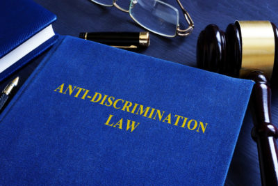 Picture of Blue Anti-Discrimination Law Book on desk with part of pen, eye glasses and gavel around it