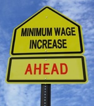 Picture of a 2 part yellow traffic sign top says Minimum Wage Increase, bottom says AHEAD