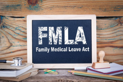 SLF Blog Picure of Chalkboard displaying FMLA Family and Medical Leave Act with a wooden plank background with medical tool and stamp