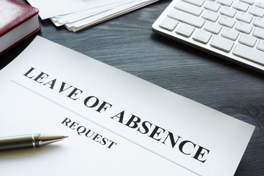 Picture of a Leave of Absence Request form with the tip of a pen the bottom of a calculator on a desk