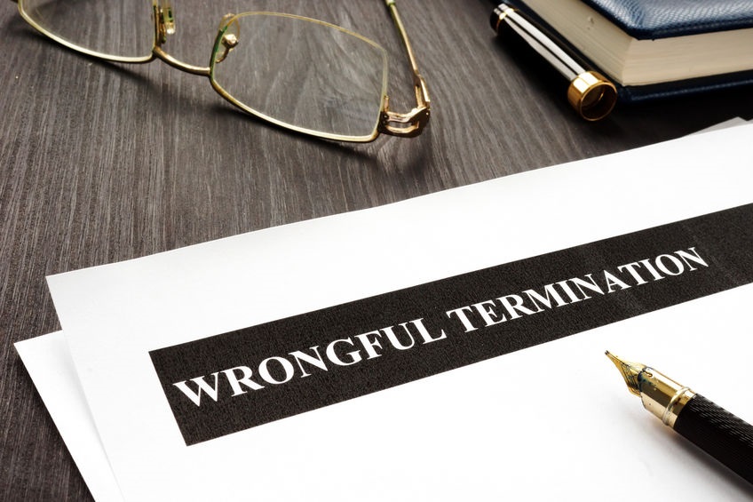Picture of a document titled wrongful termination on a desk next to wireframed glasses and a pen