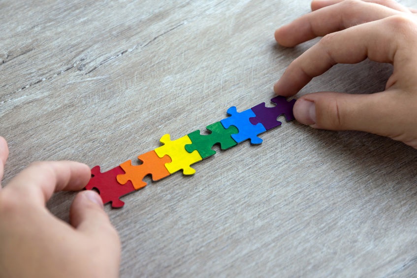 Picture of two hands putting together a string of puzzle pieces colored red, orange, yellow, green, blue and purple