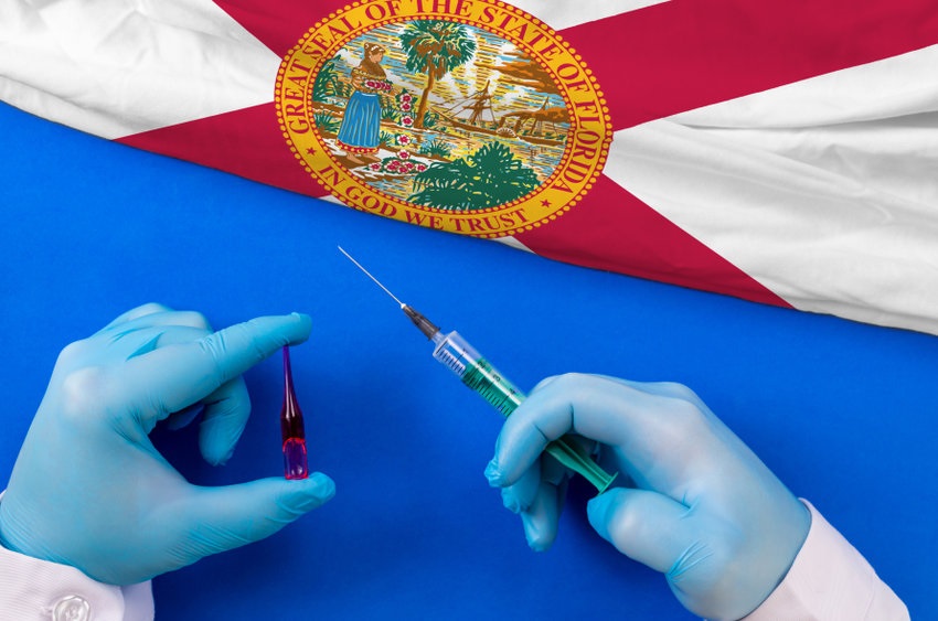 Picture of partial Florida flag above a field of blue with two blue-gloved hands holding a syringe for the COVID vaccine