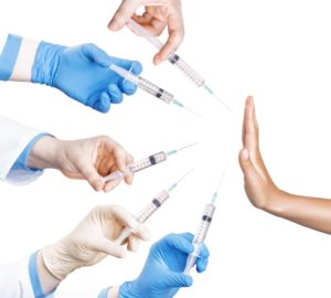 Picture of 5 hands, 3 with gloves on, reaching out with vaccination shots to a hand held in the STOP position
