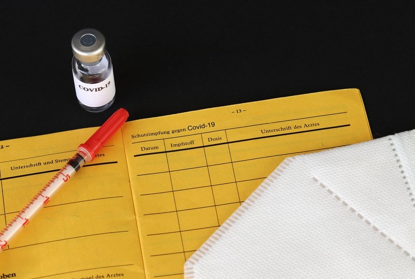 Picture of COVID-19 vaccine bottle and syringe on a yellow government form with a white mask