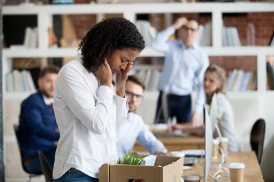 Sad african female young employee packing belongings in box at workplace got fired from job, stressed upset black worker intern leaving office on last day at work crying after unfair dismissal